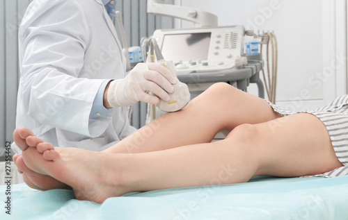 Doctor conducting ultrasound examination of patient's knee in clinic, closeup photo