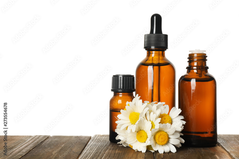 Chamomile flowers and cosmetic bottles of essential oil on wooden table against white background. Space for text Chamomile flowers and cosmetic bottles of essential oil on wooden table against white background. Space for text