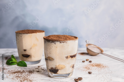 Two glasses of tiramisu cake on table against color background, space for text