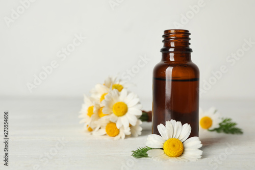 Chamomile flowers and cosmetic bottle of essential oil on wooden table against light background. Space for text