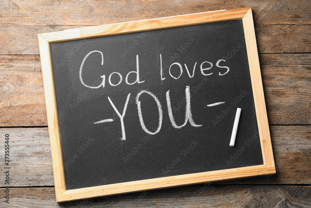 Fototapeta premium Chalkboard with words GOD LOVES YOU on wooden background, top view