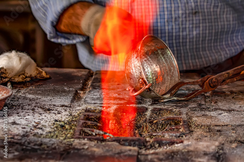 Cropped image of the traditional Turkish tinsmith covering the copper object with tin over fire.  photo