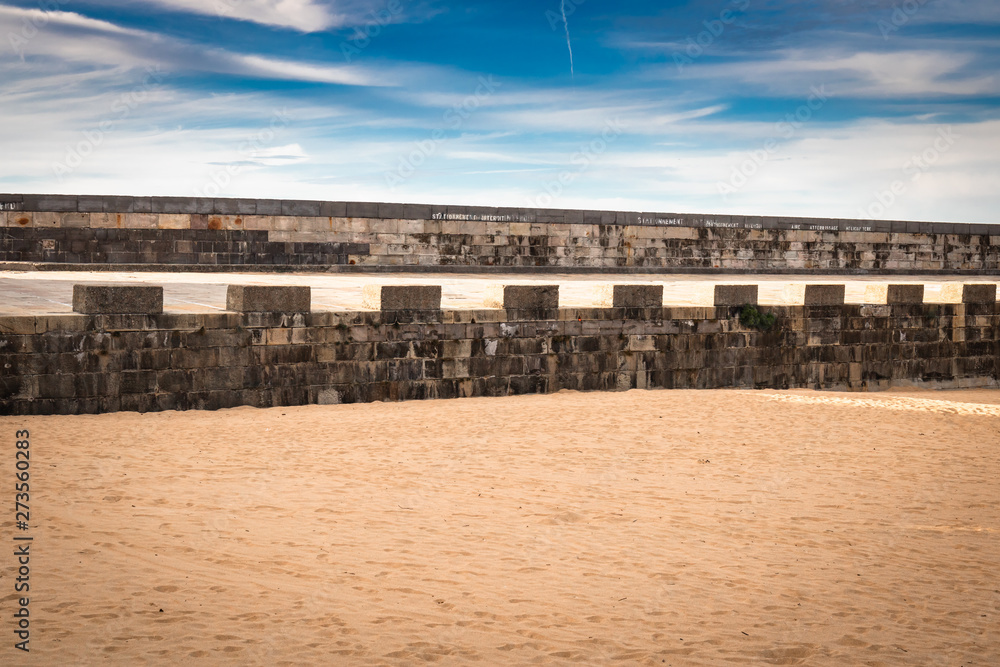 ancient medieval fortress barrier wall on sandy beach as breakwater, in sunny blue sky with clouds, creative background design