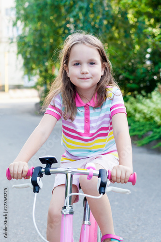 Children ride a bike near the house. A little girl on a Bicycle on a Sunny summer day. Active healthy outdoor sports for young children. Fun activity for the baby concept