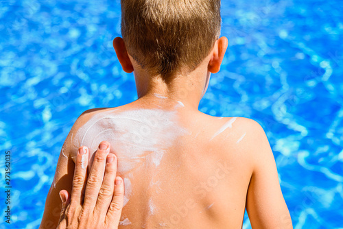 Woman spreads sunscreen on a child's back in summer to avoid sunburn.