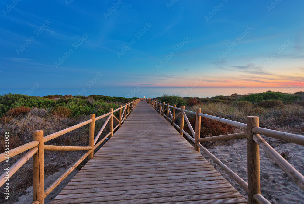 Weathered lumber path leading to calm sea during beautiful sunset