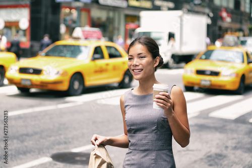 New York Asian business woman walking to work with lunch bag in the morning commuting drinking coffee cup on street with yellow cabs in the background. People commuter lifestyle.