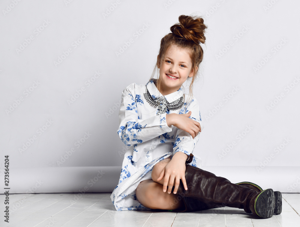 Foto Stock Teen girl kid in fashionable dress, necklace, big black boots  and with fashion hairstyle sitting on the floor posing | Adobe Stock