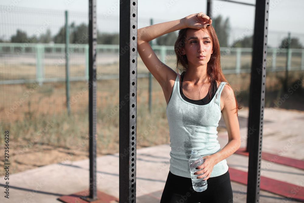 Fototapeta premium Close up portrait of young pretty caucasian fitness woman drinking water after pulling up on the horizontal bar. Breaking relax while exercise workout. Concept of health and sport lifestyle....
