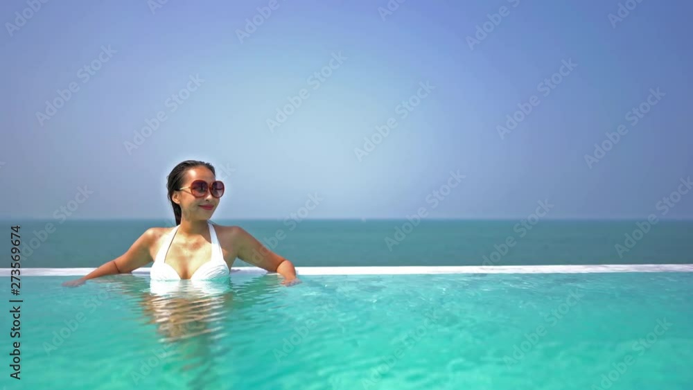 A beautiful lady sitting in a pool wearing sunglasses while smiling with the ocean behind her A beautiful lady sitting in a pool wearing sunglasses while smiling with the ocean behind her
