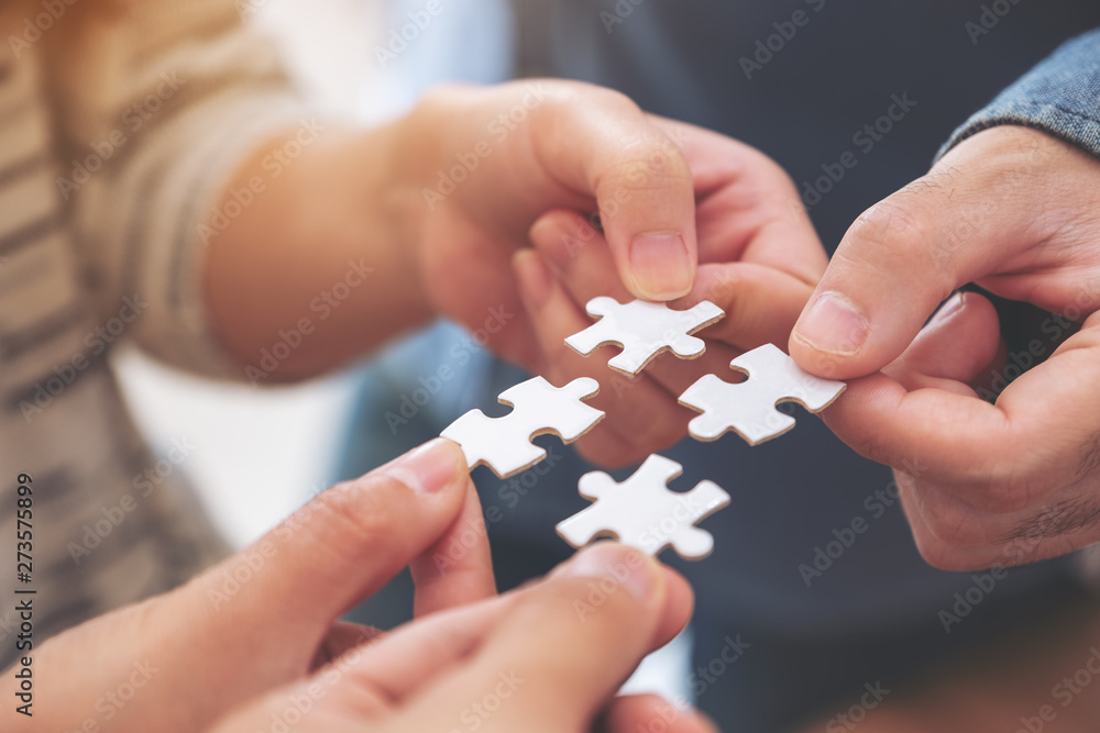 Closeup image of many people hands holding and putting a piece of white jigsaw puzzle together Closeup image of many people hands holding and putting a piece of white jigsaw puzzle together