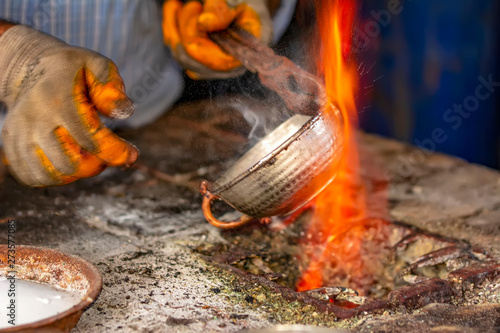Cropped image of the traditional Turkish tinsmith covering the copper object with tin over fire. 
