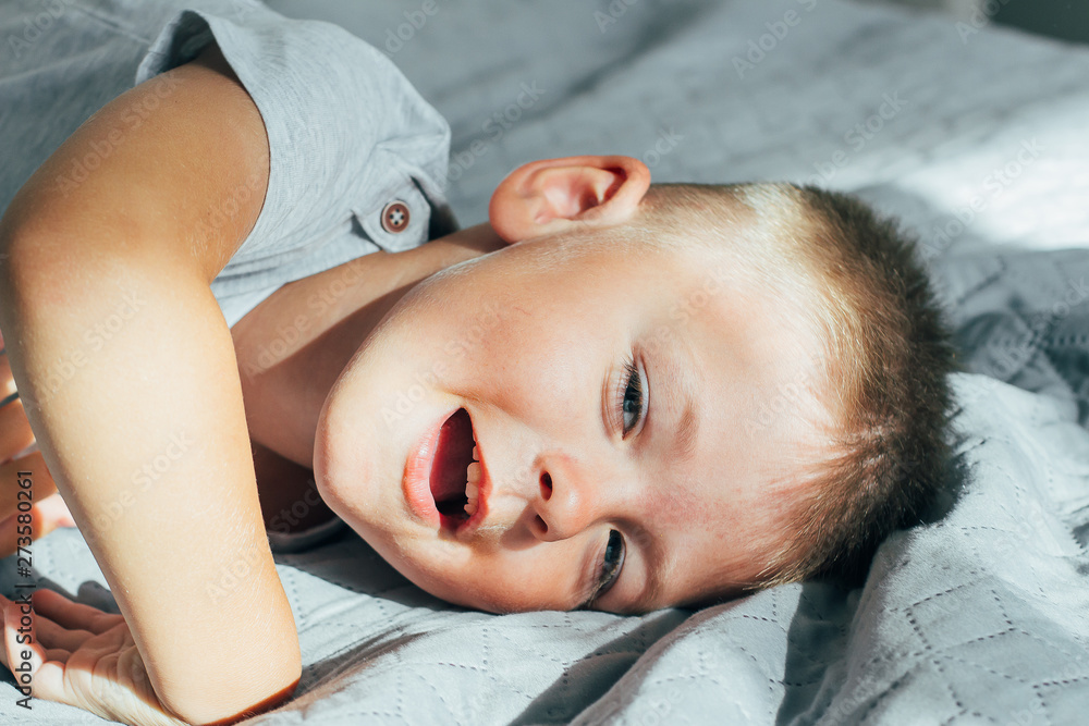 Portrait 4 or 5 years old little cute smiling and having fun boy on a bed in bedroom. A brunette boy in a grey shirt. Portrait 4 or 5 years old little cute smiling and having fun boy on a bed in bedroom. A brunette boy in a grey shirt.