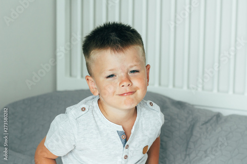 Portrait 4 or 5 years old little cute smiling and having fun boy on a bed in bedroom. A brunette boy in a grey shirt.