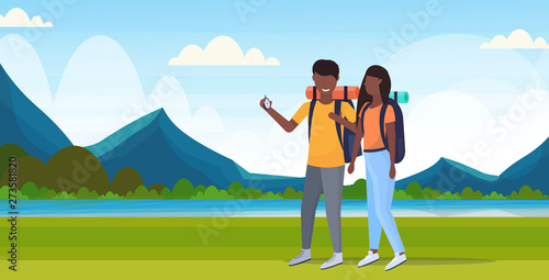 couple tourists hikers using compass searching direction hiking concept man woman african american travelers on hike mountains landscape background full length horizontal flat