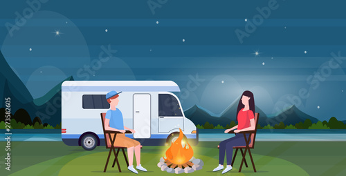 couple sitting around campfire at night near camping trailer truck caravan car man woman spendingtime togeher summer vacation concept beautful nature landscape background full length horizontal