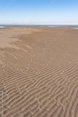 sandy beach on a clear day with wave ridge shaped patterns under clear blue sky on the coast