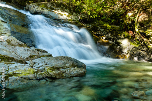 beautiful waterfall deep inside forest with water running down the creek  surrounded by green trees and moss covered rocks