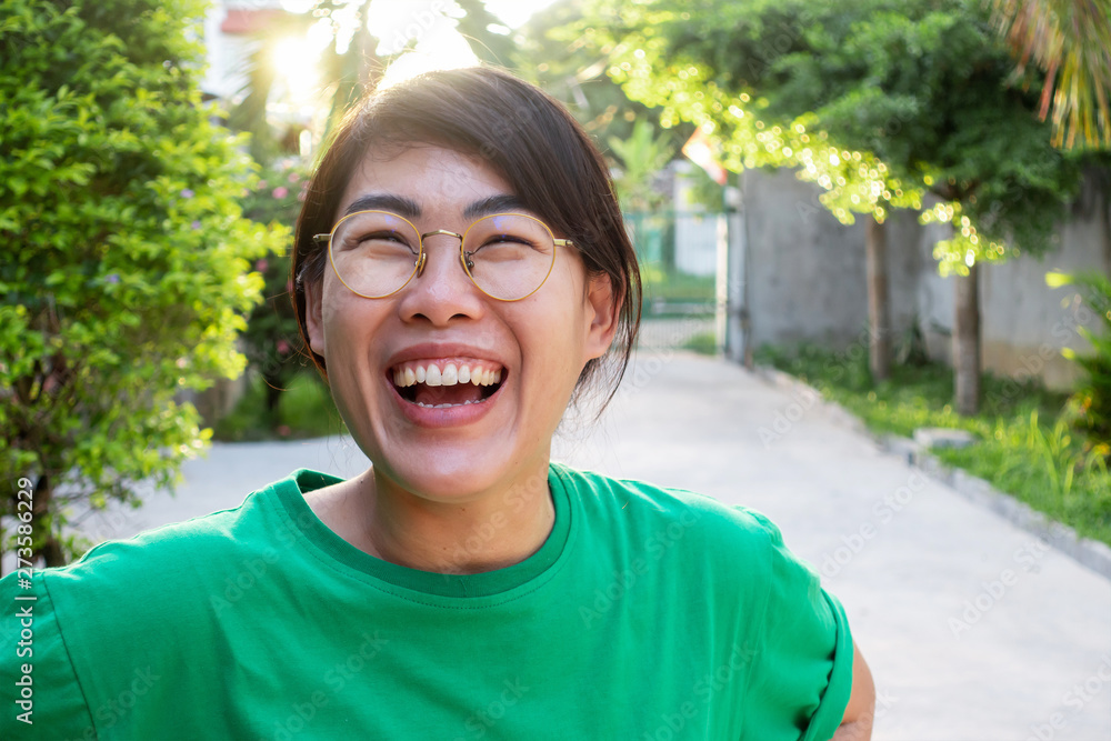 Asian woman wearing green shirt is smiling happily in the park with trees and sun light in the afternoon. Asian woman wearing green shirt is smiling happily in the park with trees and sun light in the afternoon.