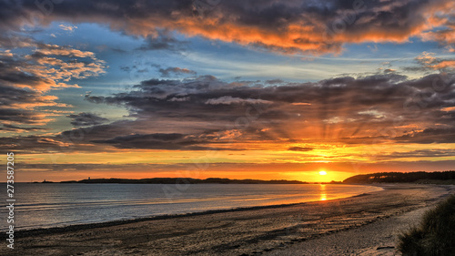 A beautiful sunset by the sea in the north of Wales near the village of Newborough. Beautiful clouds, part blue sky and in the distance a lighthouse.