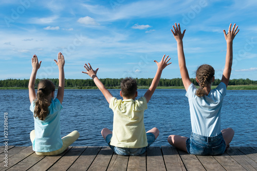 three children on the river bank near the forest do yoga