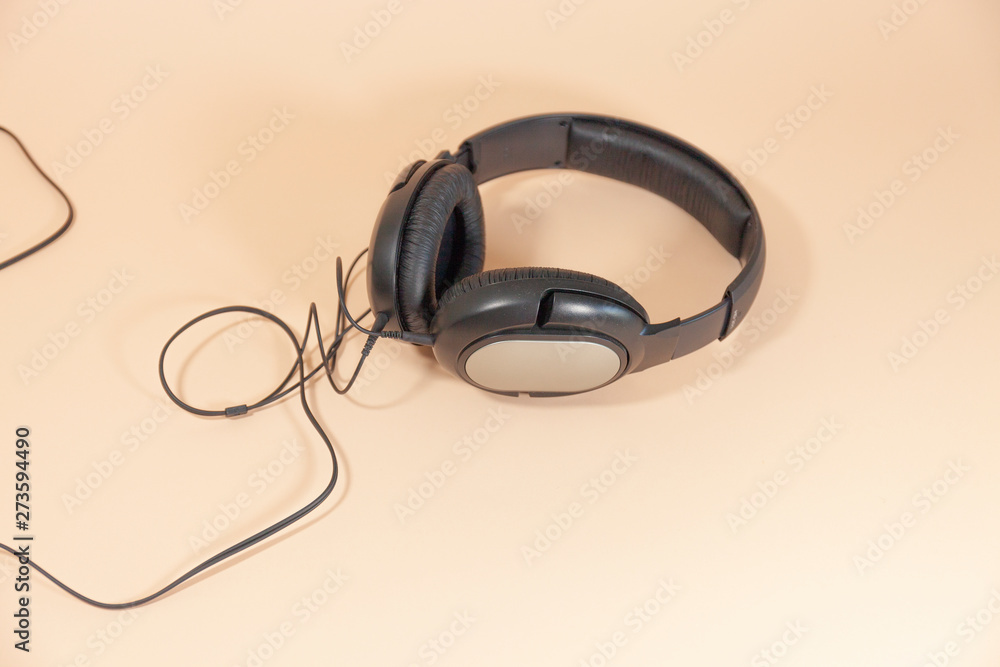 A pair of black headphones with a cord are laying on a pink surface A pair of black headphones with a cord are laying on a pink surface