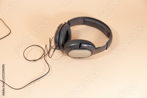 A pair of black headphones with a cord are laying on a pink surface