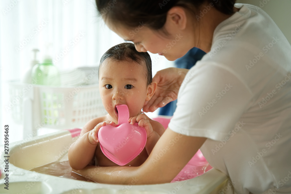 Asian beautiful mother holding little cute baby and taking a bath her child sitting in bathtub in the room. Bathtub and bath shampoo are put in the background. Clean and healthy concept. Asian beautiful mother holding little cute baby and taking a bath her child sitting in bathtub in the room. Bathtub and bath shampoo are put in the background. Clean and healthy concept.