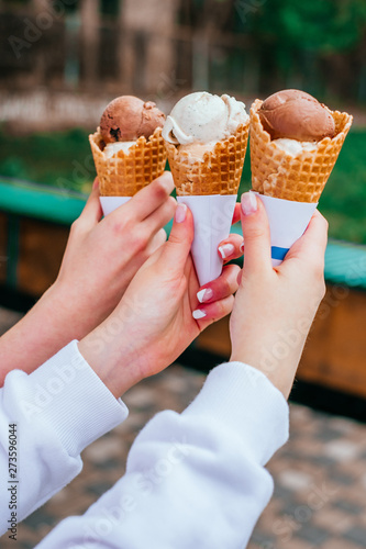 Chocolate and vanilla ice cream in waffle cups in hands of three girls friends.