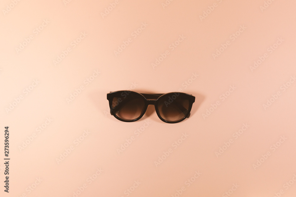 A pair of black sunglasses are laying on a pink surface