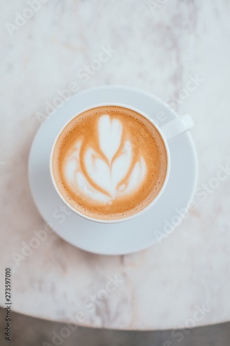 A cup of coffee with beautiful latte art in a white cup on marble table background.