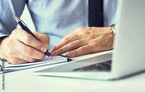 Businessman hand writing note on a notebook. Business man working at office desk. Close up of empty notebook on a blackboard with office supplies.