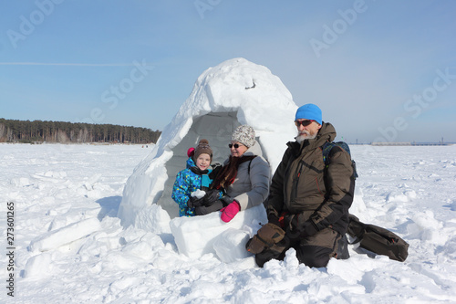 Happy grandfather, grandmother and grandson sitting near the snow on a snowy glade in winter