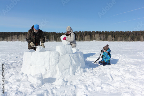 Happy grandfather, grandmother and grandson building an igloo on a snowy glade in winter, Novosibirsk, Russia