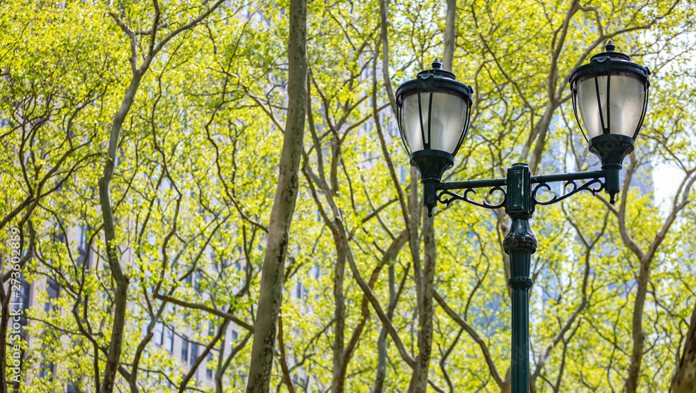 Street lamp lights against green trees foliage. New York, Manhattan downtown