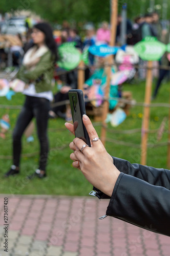 A girl in a black jacket holds a smartphone on outstretched hands. Side view