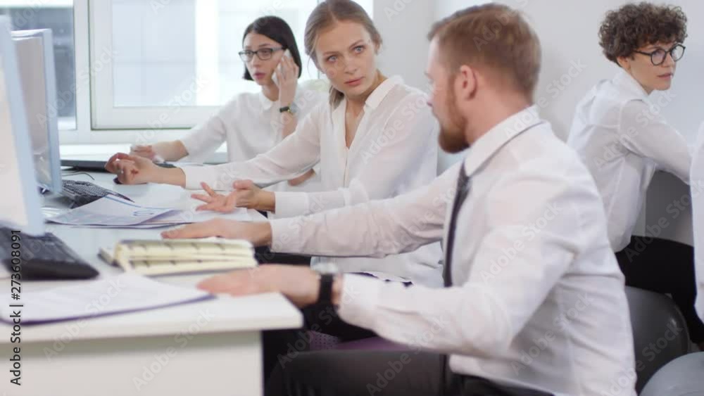 Tilt up of Caucasian businessman and businesswoman sitting on fitballs at desks, discussing charts while their female colleague talking on phone while sitting on fitball on background Tilt up of Caucasian businessman and businesswoman sitting on fitballs at desks, discussing charts while their female colleague talking on phone while sitting on fitball on background