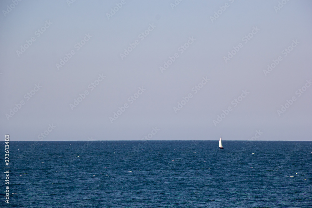 Small sailing yacht with big white sails in the open sea on the horizon Small sailing yacht with big white sails in the open sea on the horizon