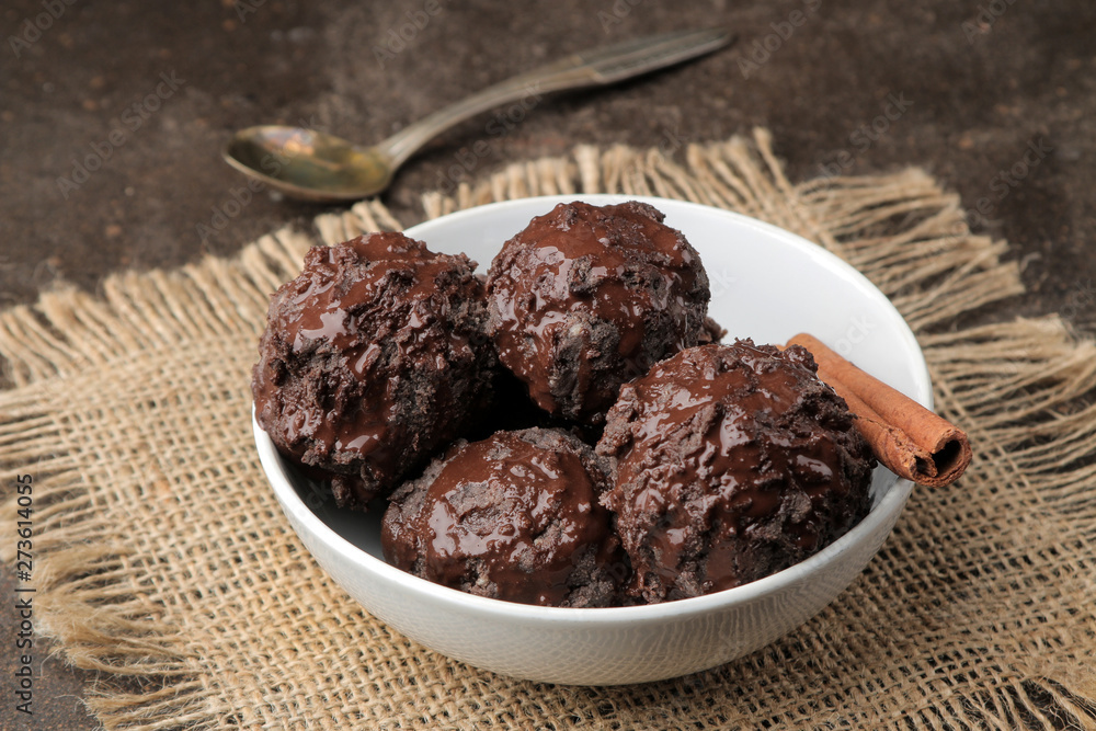 Chocolate ice cream with liquid chocolate with a cinnamon stick and coffee beans on a dark background. Chocolate ice cream with liquid chocolate with a cinnamon stick and coffee beans on a dark background.