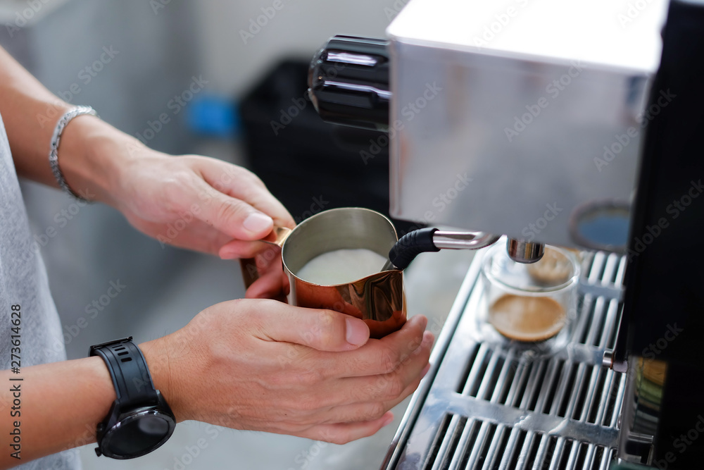 Barista steaming milk in pitcher, reaches proper temperature degrees Fahrenheit for making coffee latte 