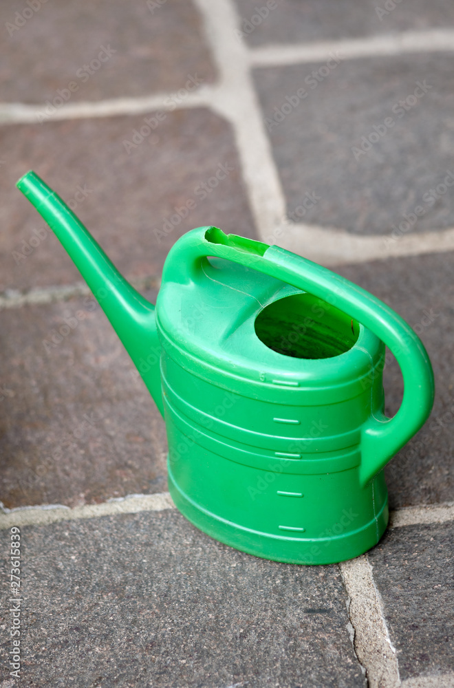 A damaged old green watering can is standing on the pavement stones in the garden A damaged old green watering can is standing on the pavement stones in the garden