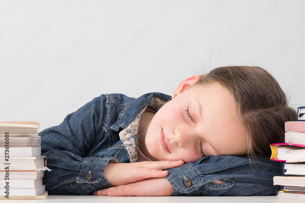 School time routine. Portrait of female kid sleeping soundly on table among book stacks. White background.
