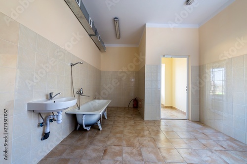 Interior of spacious light hospital or kindergarten bathroom with white bathtub, sink, air ventilation duct and tiled floor and walls.