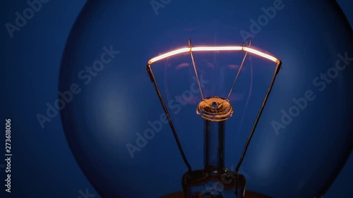 flickering tungsten filament of classic incandescent lamp on blue background close up. bad electrical contact immitation photo