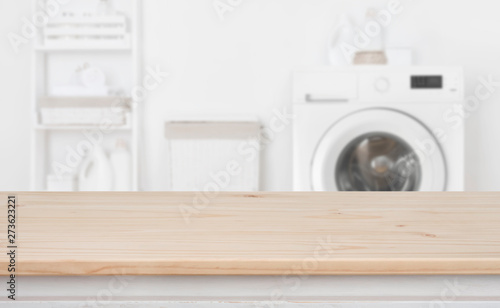 Photo Wooden table in front of defocused washing machine and laundry