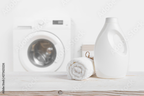 Laundry detergent bottle on wooden table over defocused washing machine photo