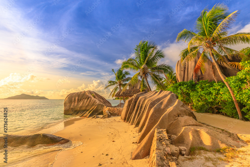 Anse Source d'Argent at sunset. Seychelles, La Digue. Landscape of palm trees and rock stone of granite blouders. Sunlight over the horizon. Source d'Argent Beach is paradise of Seychelles Islands.