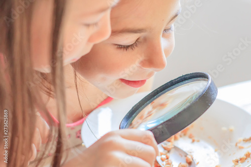 Children are considering a magnifying glass leftover food on a plate