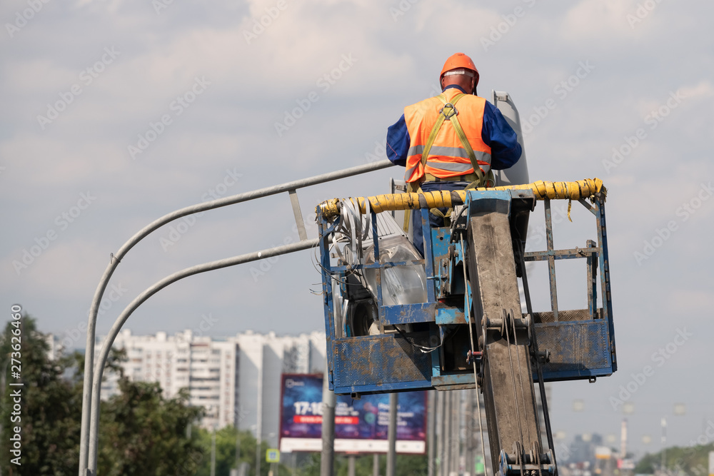 Worker in lift bucket during installation of metal pole with street lamp, street light pole with double head.