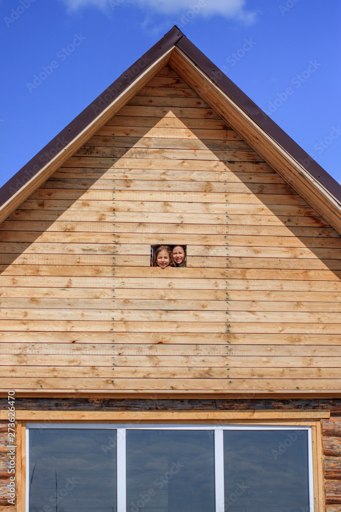 Children's faces in a small window in the attic of a wooden house